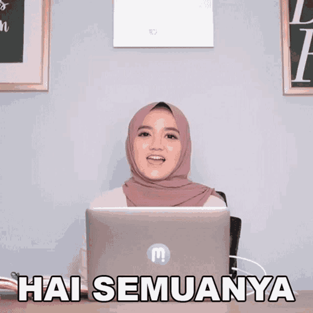 a woman wearing a hijab is sitting in front of a laptop with the words hai semuanya written on it