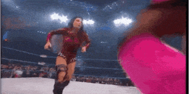 two women are wrestling in a ring and one is wearing a red outfit .