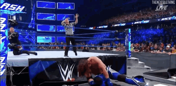 a wrestler is laying on the ground while a referee looks on