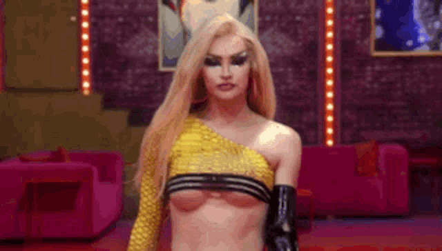 a woman in a yellow top and black gloves is standing in front of a pink couch .