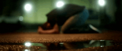 a person is kneeling down in a puddle of water on the ground at night .