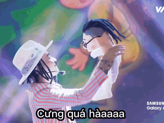 a man with dreadlocks is holding a puppet with a samsung galaxy advertisement behind him