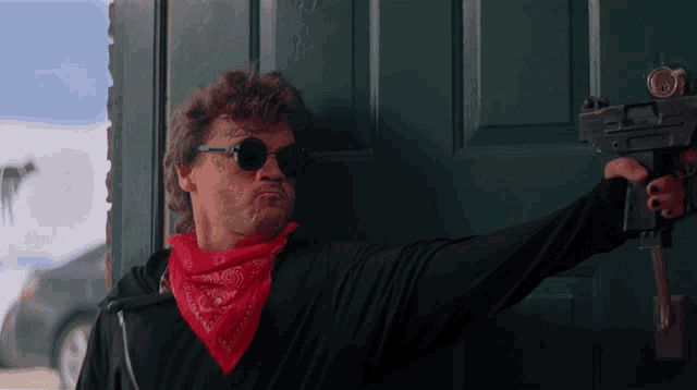 a man wearing sunglasses and a bandana holds a gun