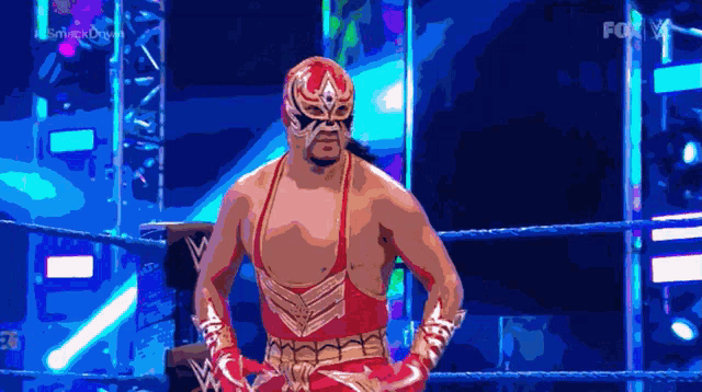 a wrestler in a red and gold outfit is standing in a ring with a fox logo behind him