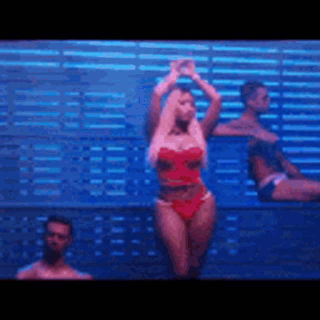 a woman in a red bikini is dancing on a stage with two men behind her