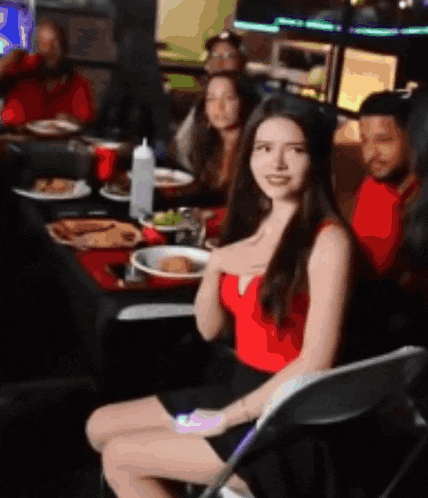 a woman in a red top sits in a chair in front of a table full of food