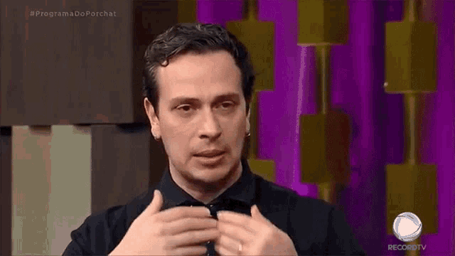 a man in a black shirt and tie is on a television show .