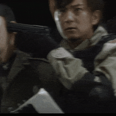 a man in a camouflage jacket is holding a gun in a dark room
