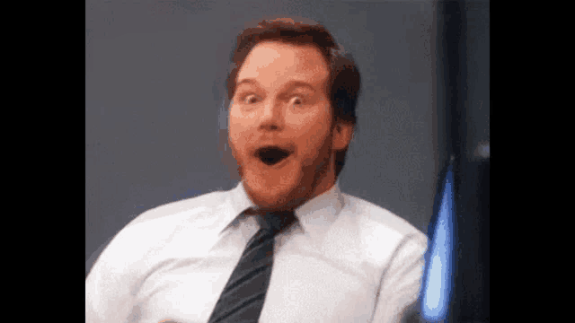 a man in a white shirt and black tie is making a surprised face .