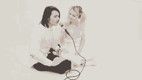 a man is singing into a microphone while a woman sits next to him .