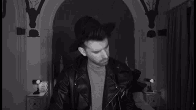a black and white photo of a man wearing a leather jacket and hat