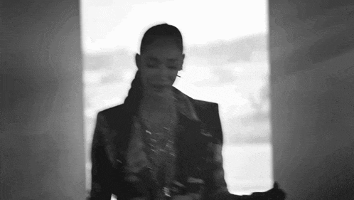 a black and white photo of a woman in a suit standing next to a window .