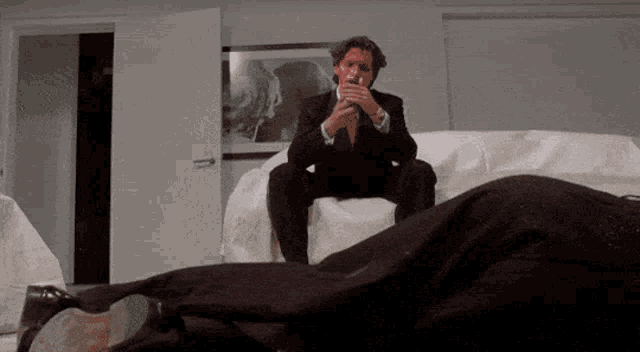 a man in a suit sits on a couch next to a woman laying on a bed