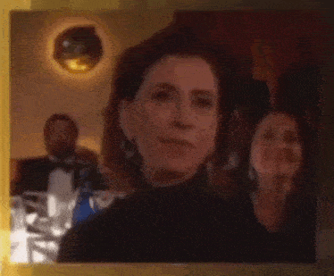 a woman in a black turtleneck is sitting at a table with a man in a tuxedo in the background .