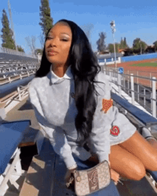 a woman is sitting on a bench in a stadium with a purse on her lap .