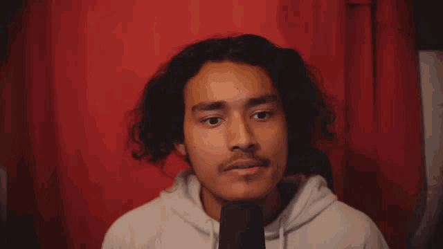 a young man with curly hair and a mustache is wearing a white hoodie