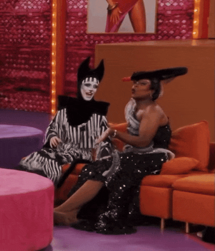 two drag queens are sitting on a couch and one is wearing a zebra print dress