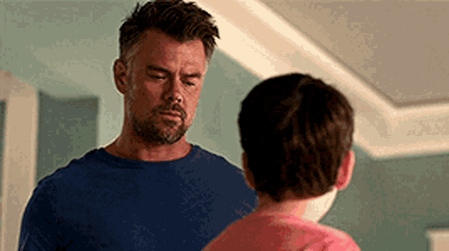 a man and a boy are standing next to each other in a room . the boy is wearing a pink shirt .