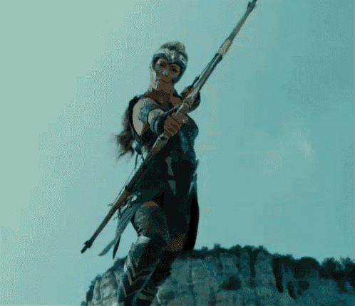 a woman in a warrior costume is holding a spear while standing on top of a mountain .