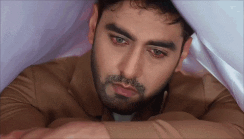 a man with a beard is laying under a blanket and looking down