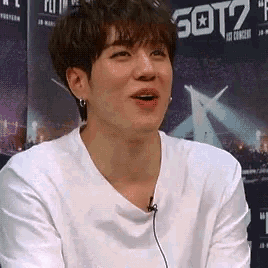 a young man wearing a white t-shirt is sitting in front of a sign that says got7 .