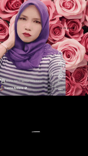 a woman wearing a purple scarf and a striped shirt stands in front of pink roses