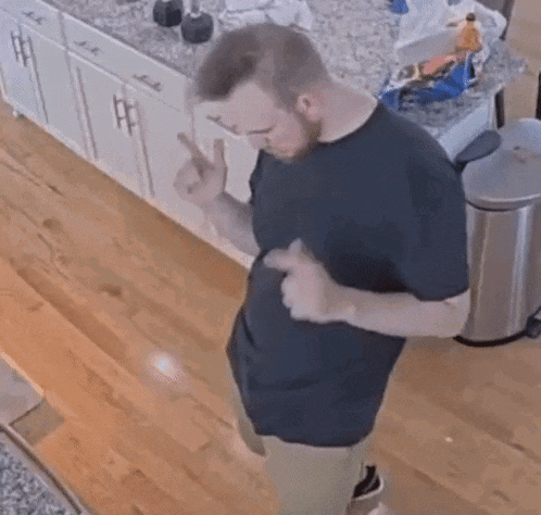 a man in a black shirt is standing in a kitchen .