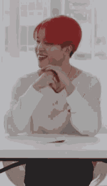 a young man with red hair is sitting at a table with his hands folded .