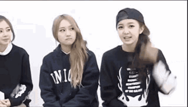 a group of young women are sitting next to each other . one of the girls is wearing a baseball cap .