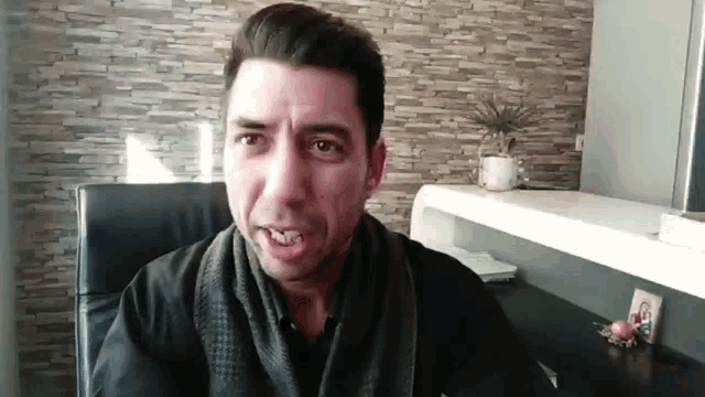 a man is sitting in a chair with a scarf around his neck and making a funny face .
