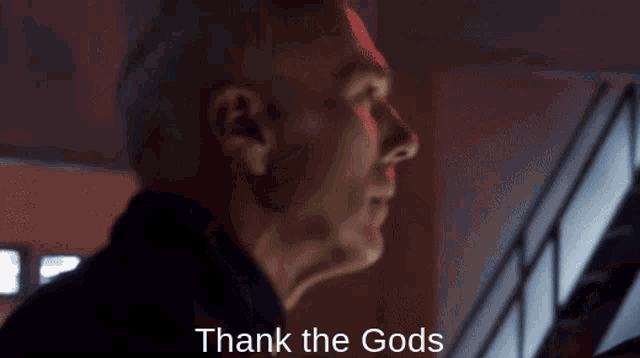 a man in a dark room with the words thank the gods above him