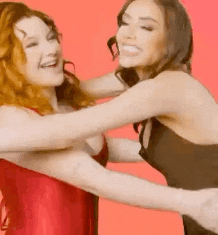 two women are hugging each other and laughing while standing next to each other on a red background .