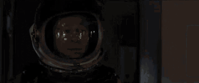 a man in an astronaut 's helmet is looking at something in a dark room .