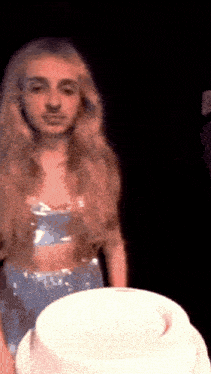 a woman in a blue dress is standing in front of a white cake