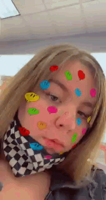 a girl with colorful smiley faces on her face and a checkered scarf around her neck .