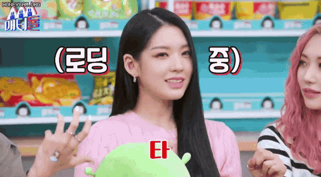 a girl in a pink sweater is holding a green stuffed turtle with korean writing on it