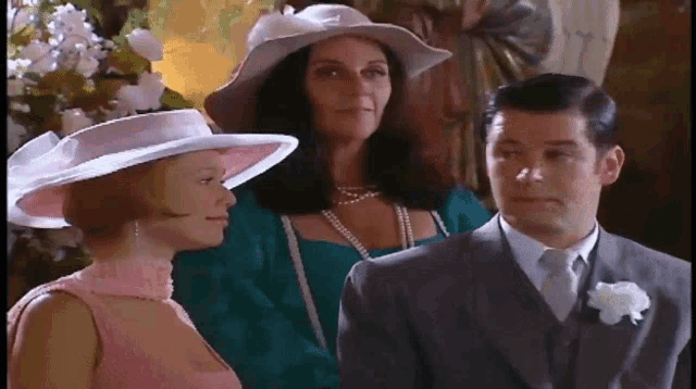a man in a suit and tie is standing next to a woman in a pink dress and a woman in a white hat .