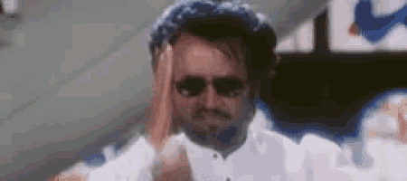 a man wearing sunglasses and a white shirt is scratching his head .