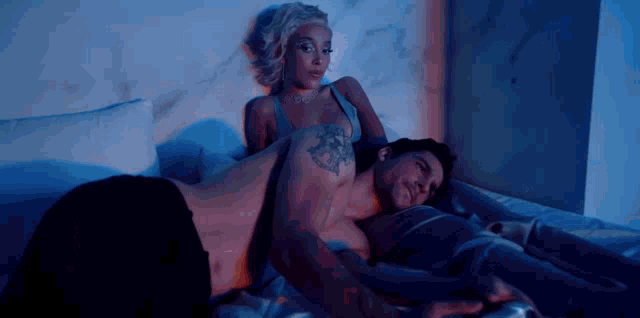 a man and a woman are laying on a bed . the man has a tattoo on his arm .