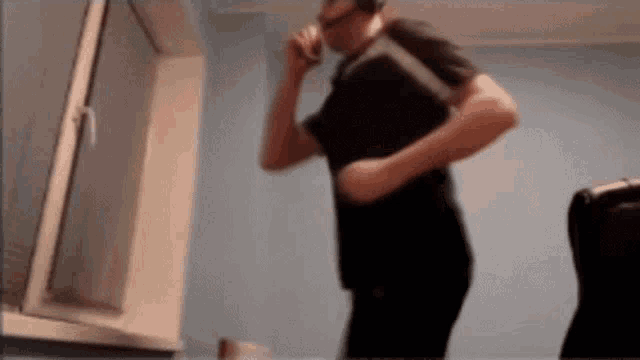 a man in a black shirt is standing in front of a window talking on a cell phone