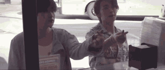 two men are standing next to each other in a restaurant . one of the men is pointing at the camera .