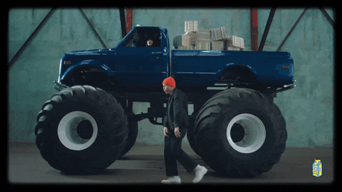 a man in a red hat walks past a blue monster truck