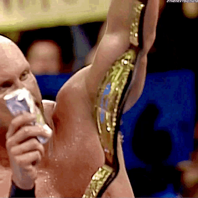 a man is drinking from a bottle while wearing a wrestling belt