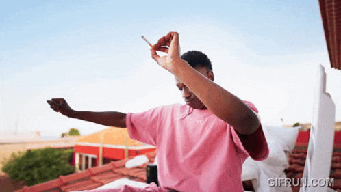 a man in a pink shirt is holding a cigarette in his hand with gifrun.com written below him