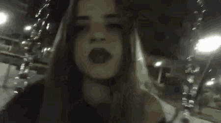 a girl with long hair and red lipstick is standing in a dark room at night .