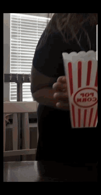 a woman is holding a striped container of popcorn
