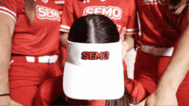 a woman wearing a somo visor is surrounded by other women in red jerseys