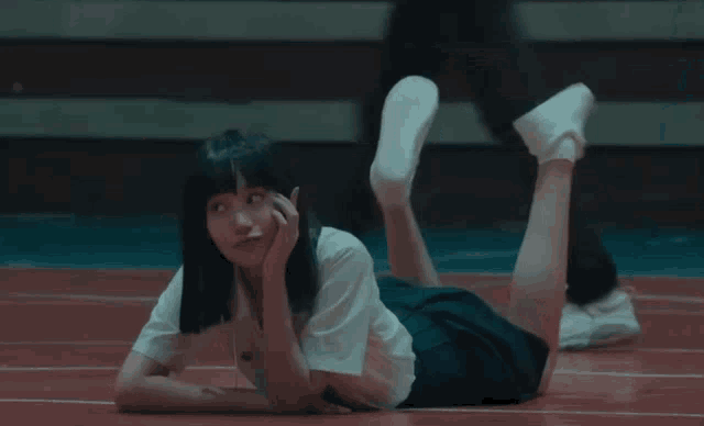 a girl in a white shirt and black skirt is laying on the floor with her legs crossed
