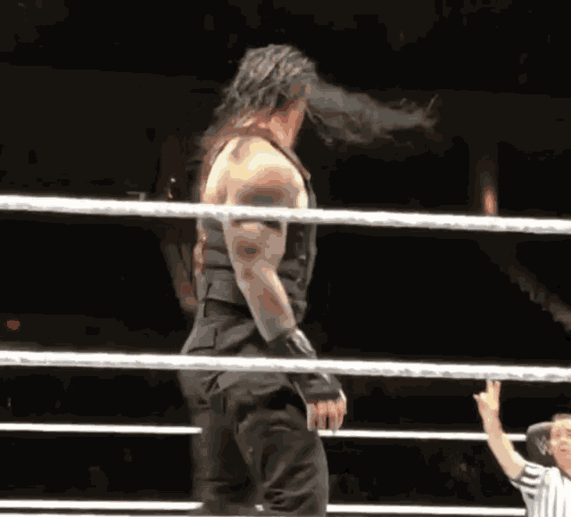 a wrestler with long hair is standing in a ring with a referee