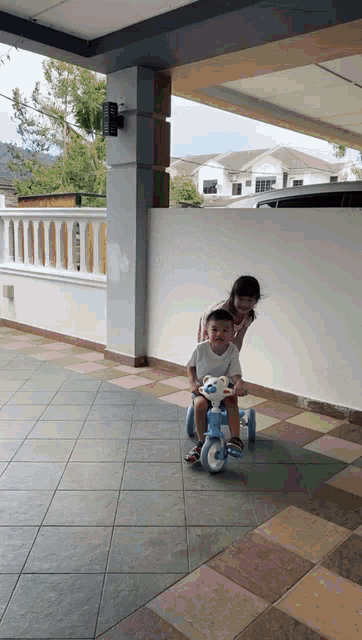 a little girl pushes a little boy on a toy tricycle
